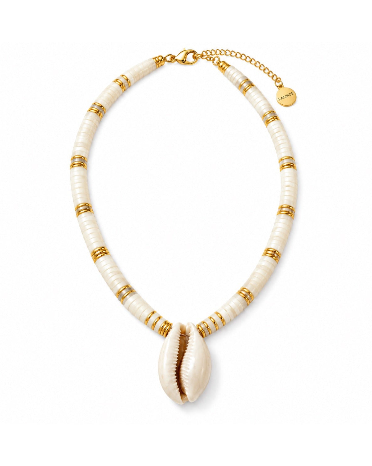 A shell-beaded necklace featuring cream-colored shell beads separated by gold spacer rings, with a large cowrie shell pendant at the center and a gold chain extender with a brand tag.