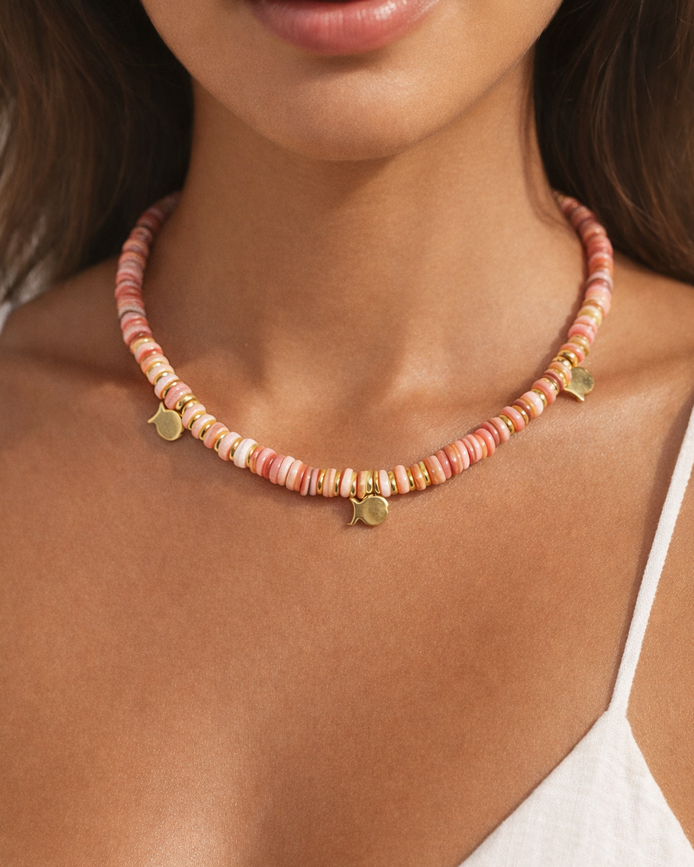 Necklace with pink beads and gold accents worn by a person