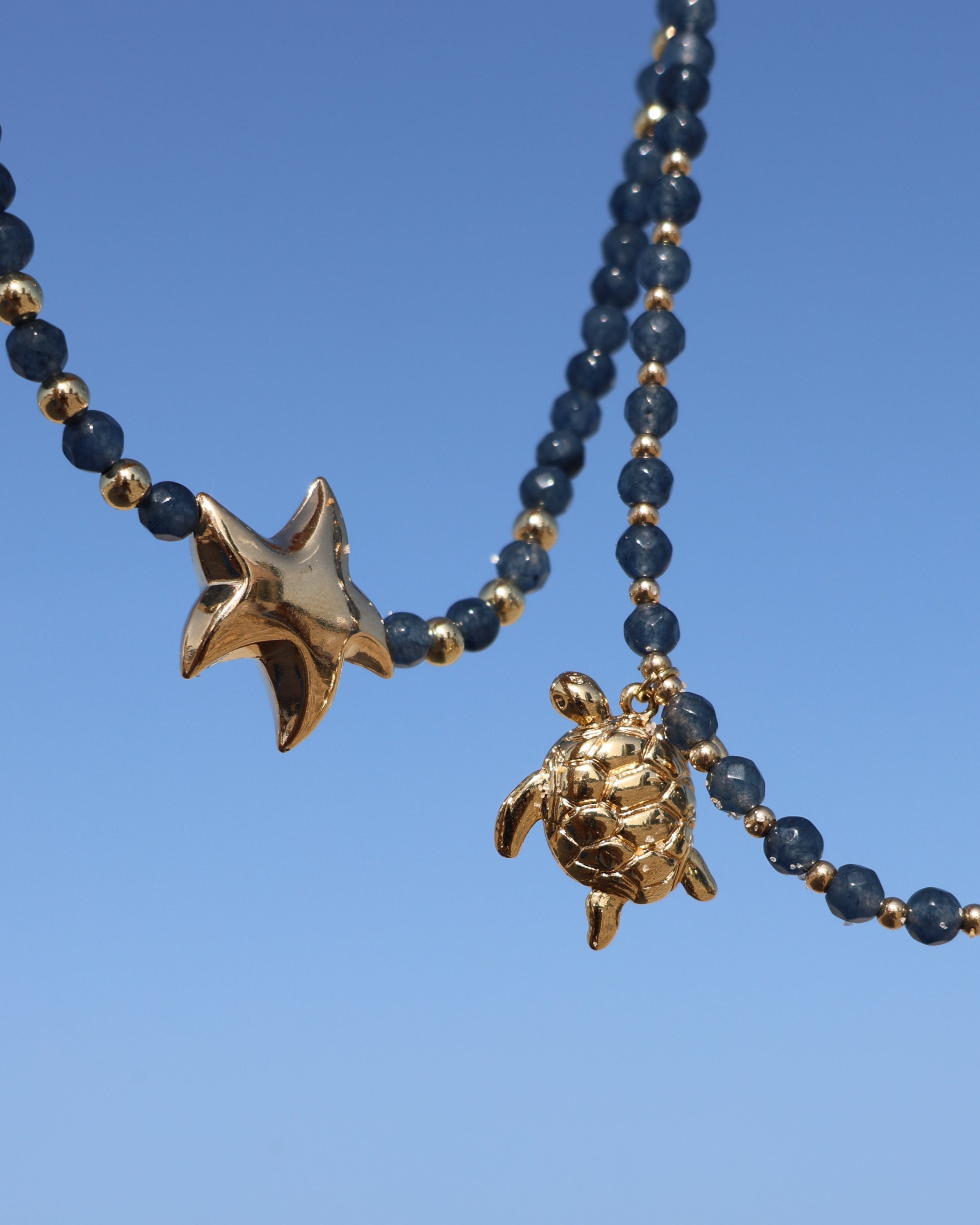 Two necklaces with star and turtle pendants on a clear blue background