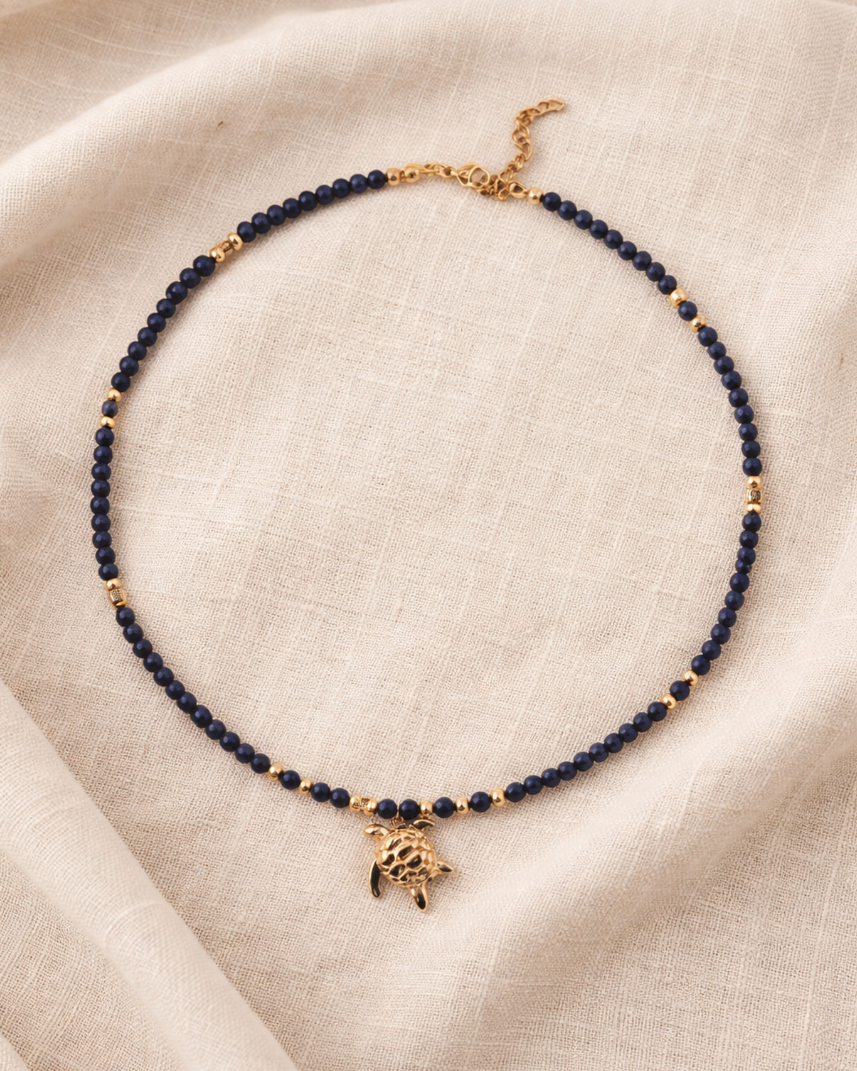 Necklace with blue beads and gold turtle charm on beige fabric