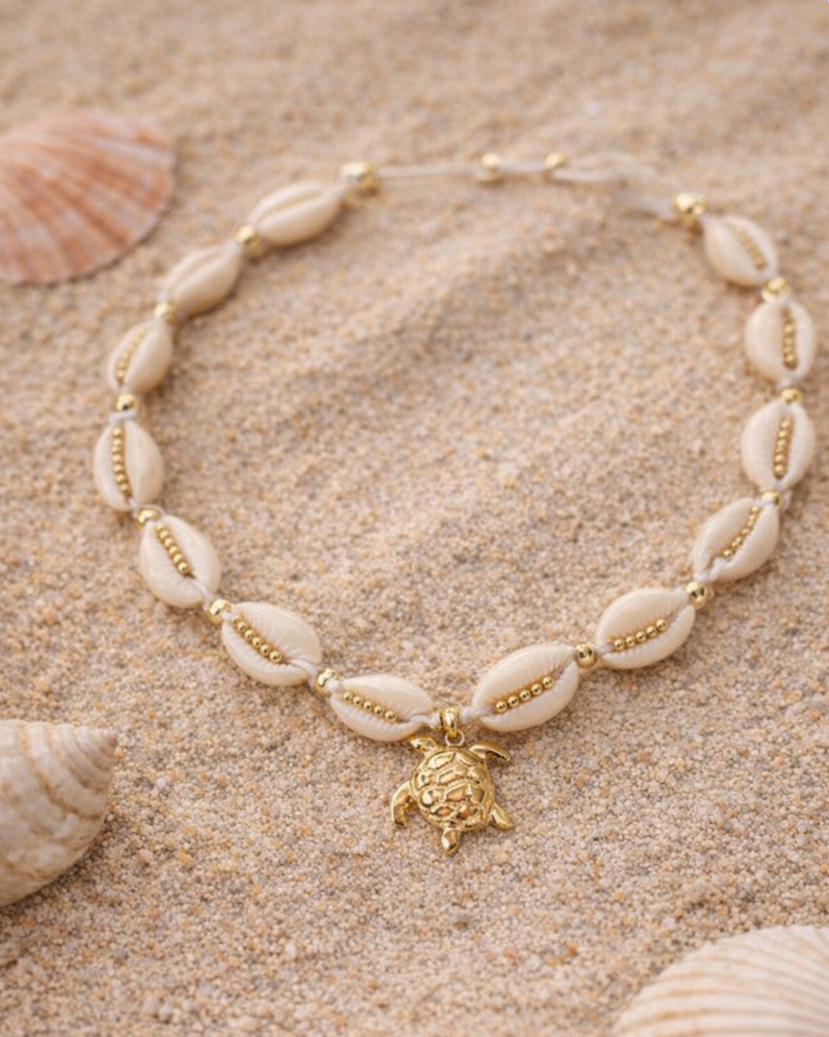 Shell necklace with a turtle pendant on sand with seashells