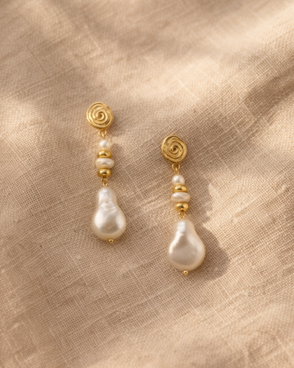 Pair of pearl earrings with gold accents on a beige fabric background