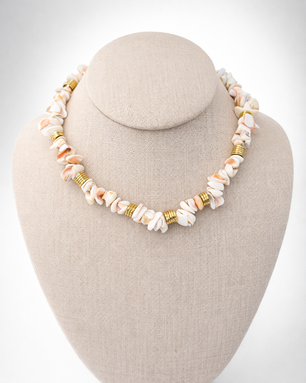 Necklace with shell and gold beads on a beige bust against a white background