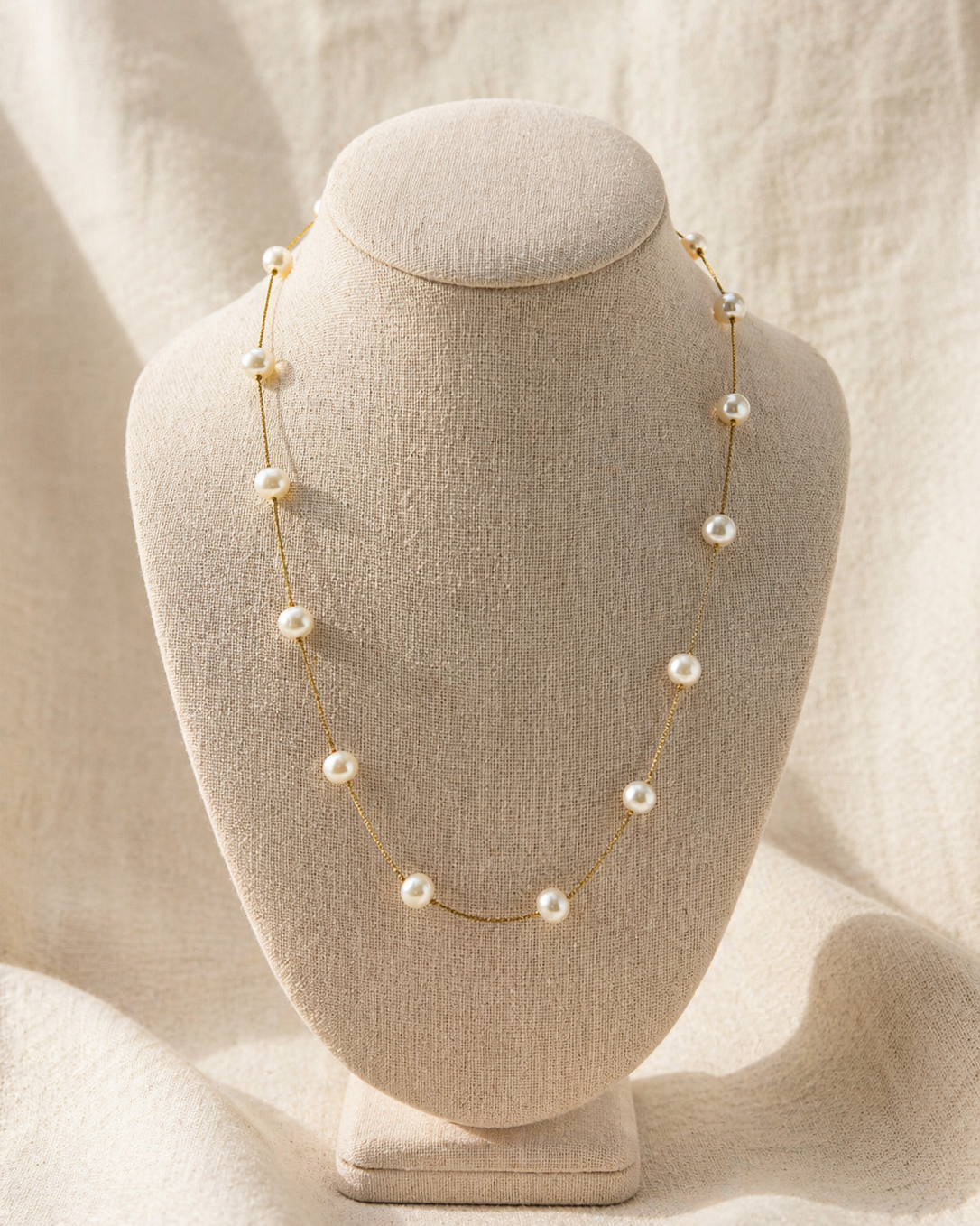Pearl necklace on a mannequin bust against a soft beige background
