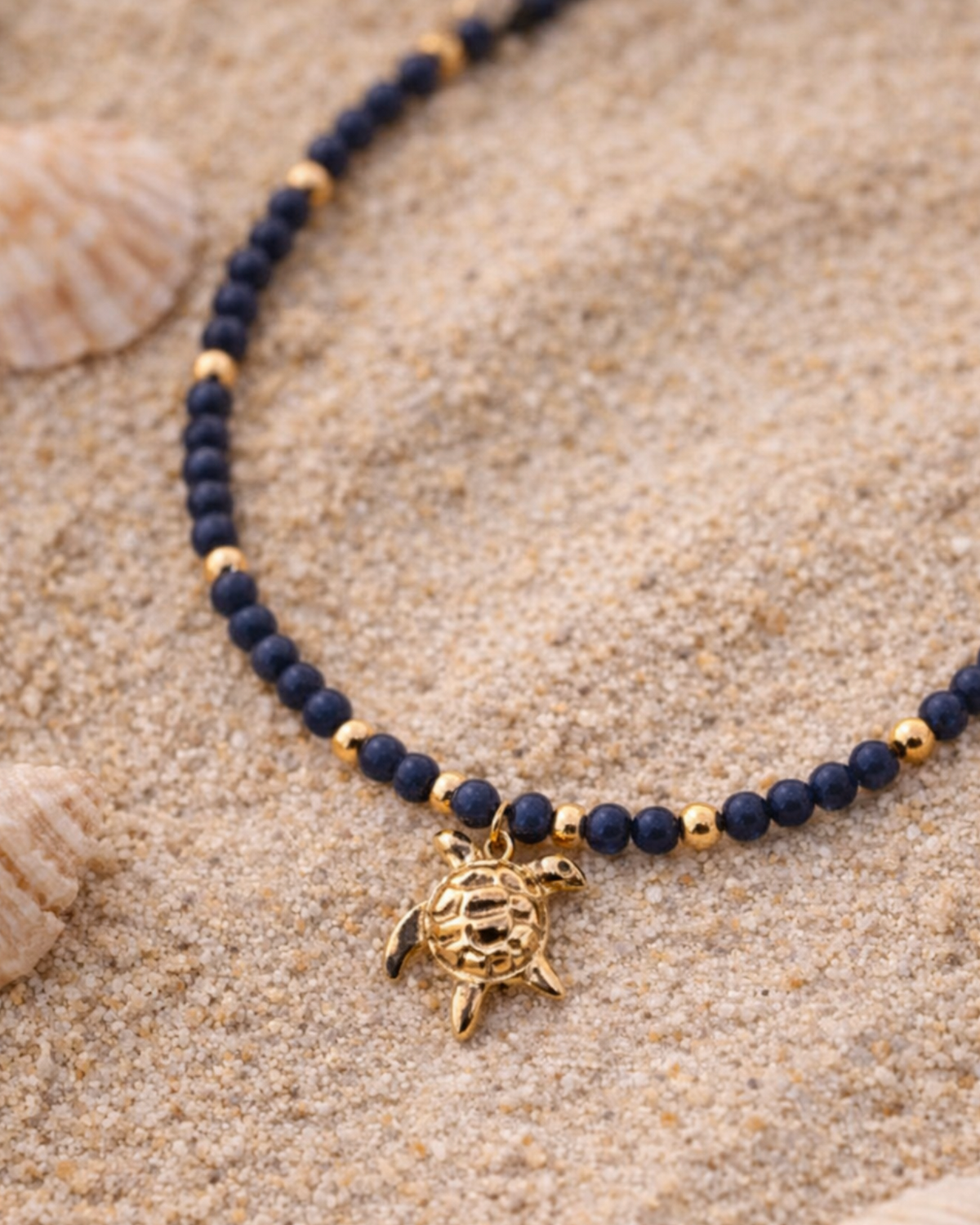 Necklace with navy beads and gold turtle charm on sand