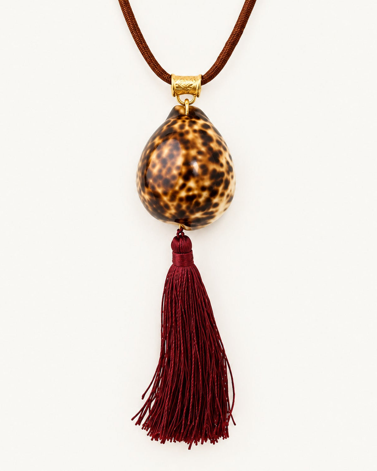 Discover the Maris Cowrie Necklace with a natural shell, adjustable brown paracord, burgundy tassel, and vintage brass details. Handmade