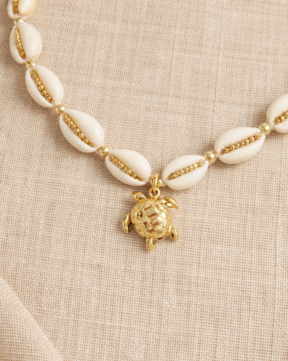 Necklace with white shell beads and a gold turtle charm on a beige fabric background