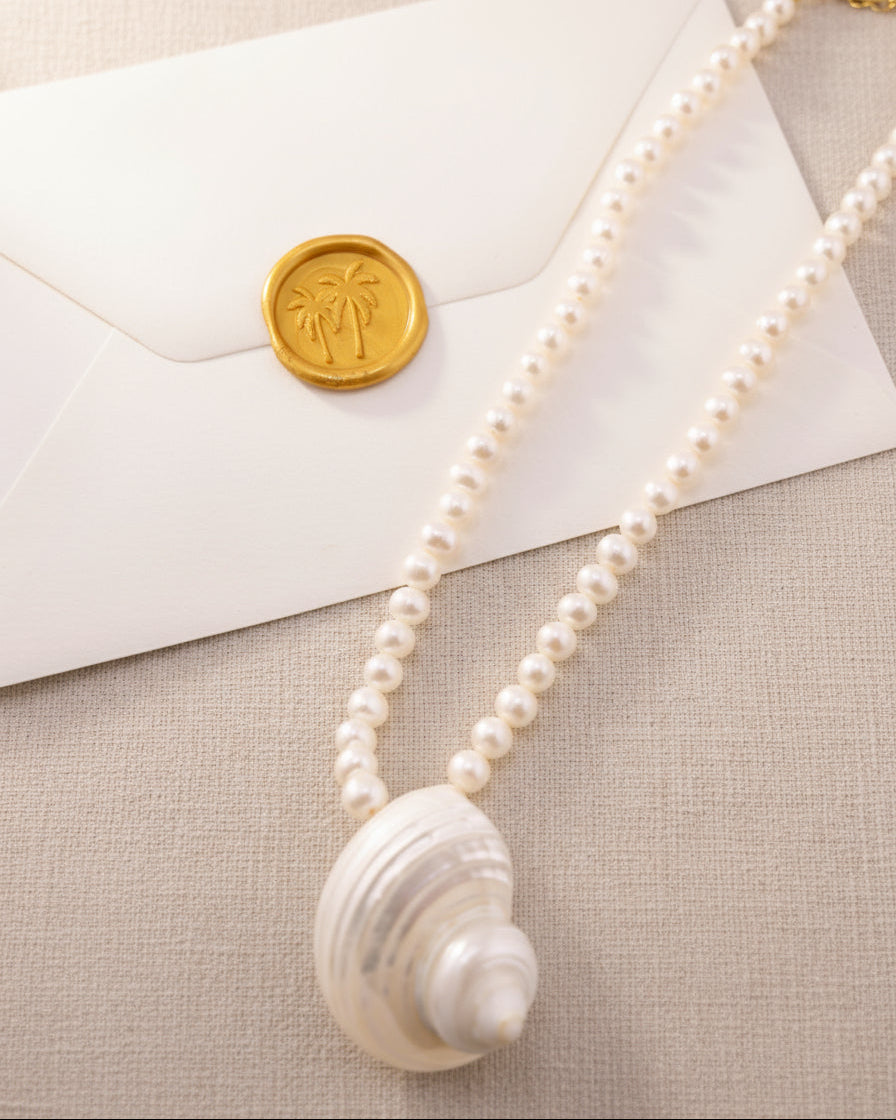 Pearl necklace with a shell pendant on a textured surface with an envelope and wax seal.