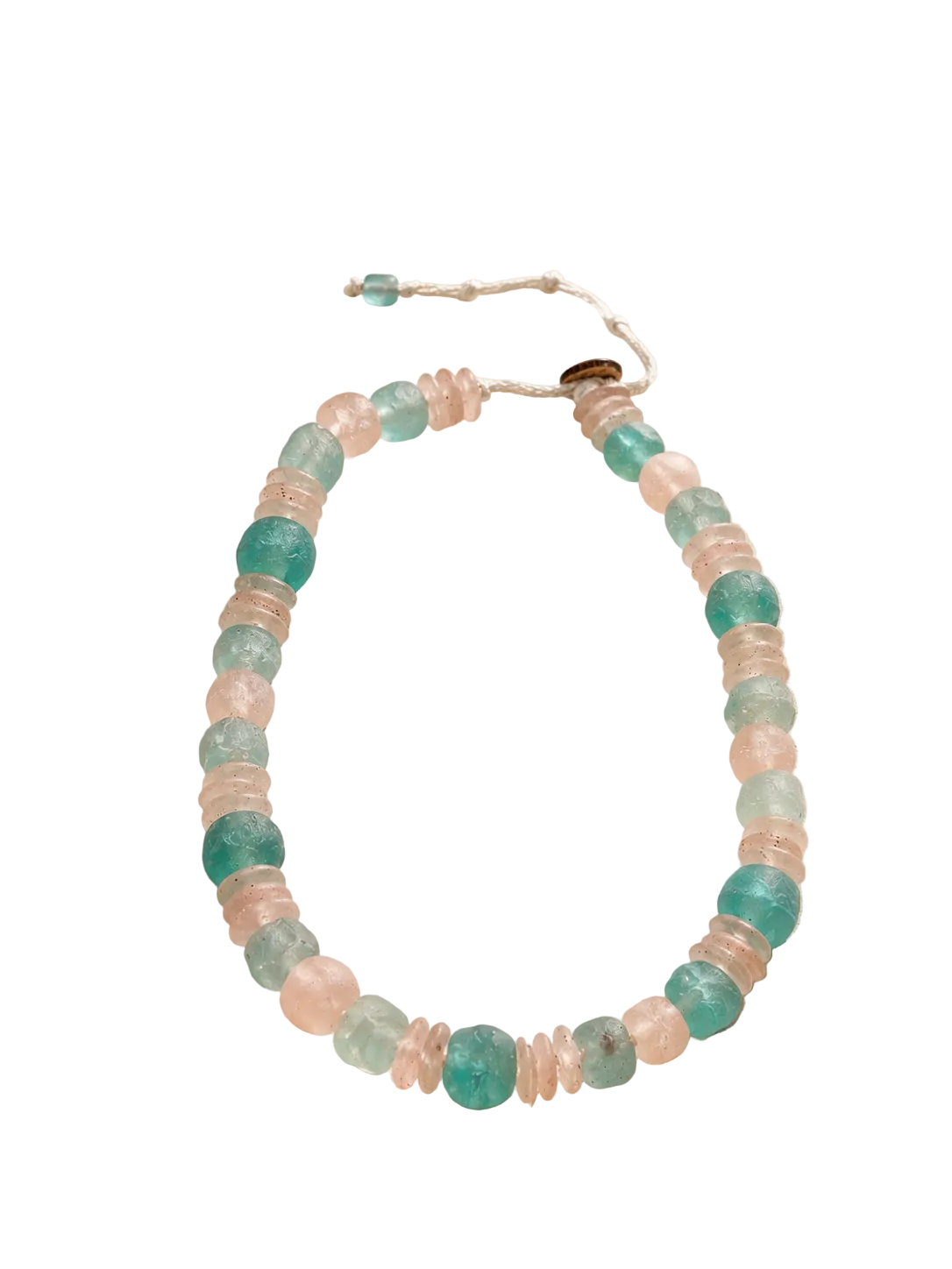 A beaded necklace made of translucent aquamarine and blush pink round beads, displayed on a textured beige stone surface with a blurred ocean and seashell background.